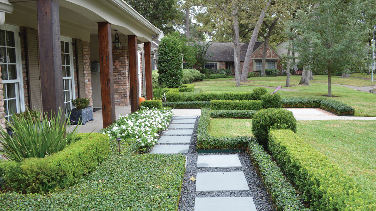 Front of a home with perfectly trimmed shrubs and paver walkway