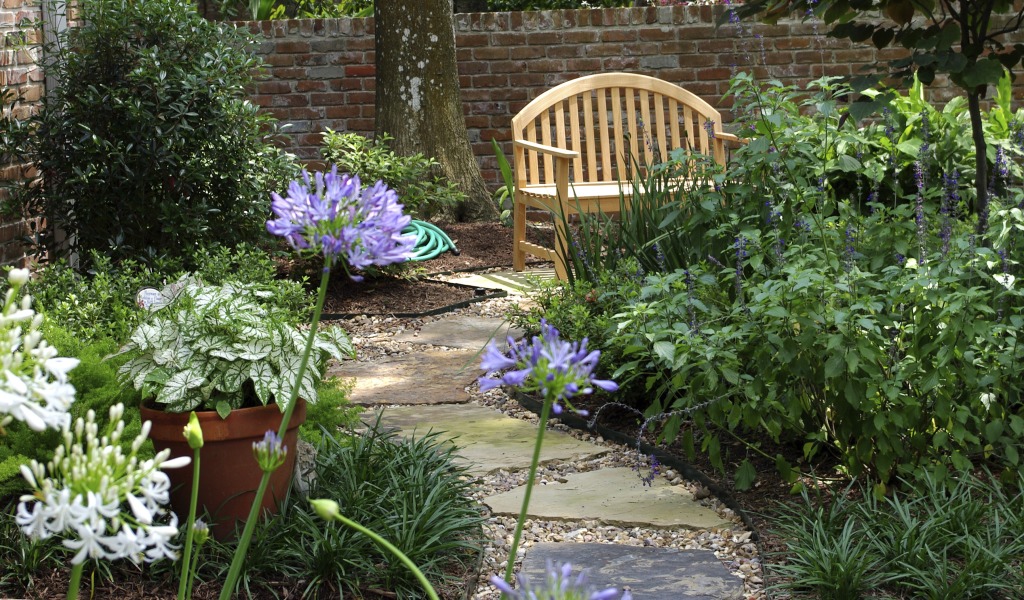 Wooden bench and stone path with flowers designed as part of a luxury backyard landscape and garden